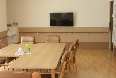 木製テーブルとテレビを備えた介護施設の共用リビング・談話室