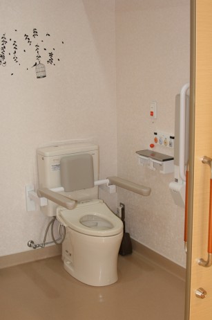 介護対応トイレ。温便座付きの洋式便器と手すりが備わっている。